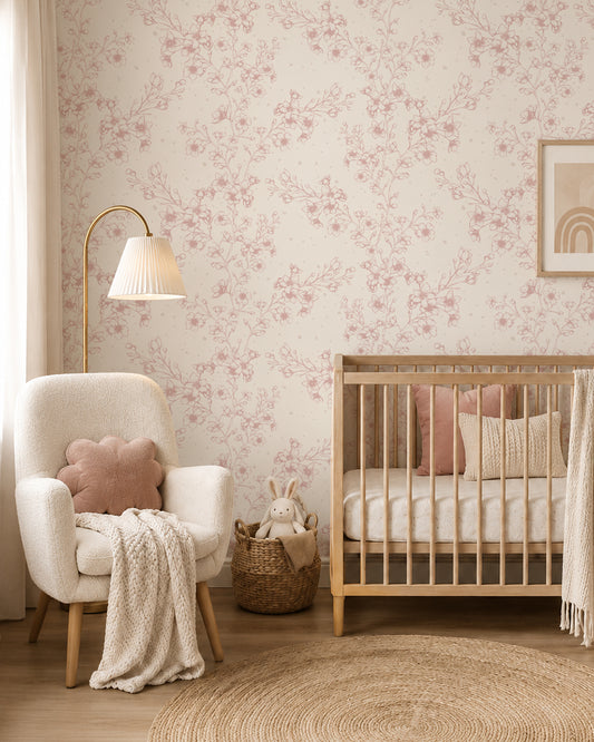 Blossom Whisper Dusty Rose floral wallpaper in a soft nursery with a natural wood crib, cream armchair and blush accents.