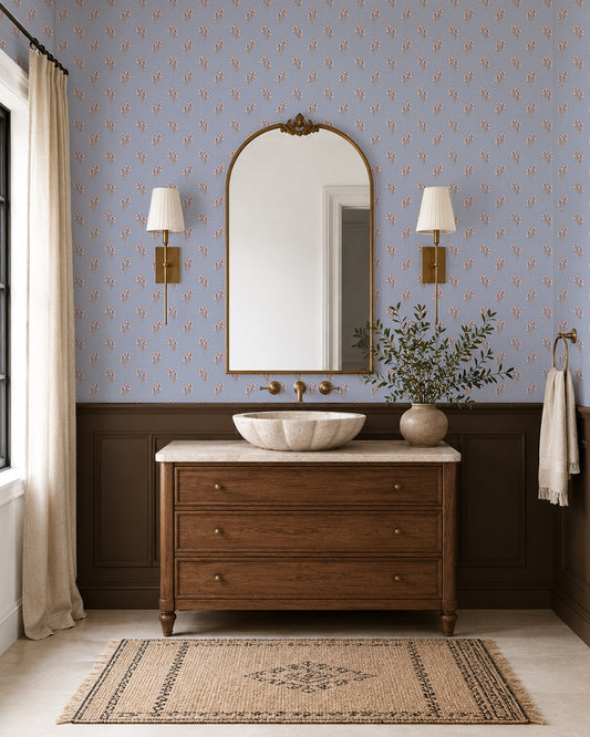 Foraged Bloom Dusty Blue wallpaper in an elegant bathroom with a wood vanity, brass sconces and dark wainscoting.
