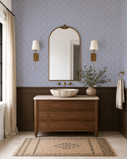 Foraged Bloom Dusty Blue wallpaper in an elegant bathroom with a wood vanity, brass sconces and dark wainscoting.